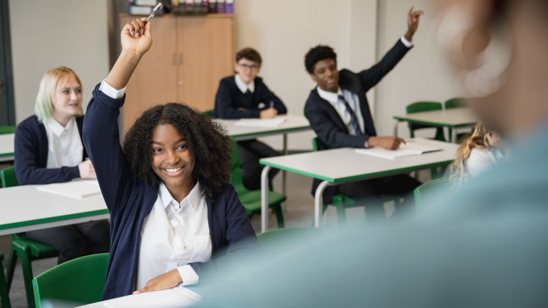 Diverse group of enthusiastic students raising their hands to participate in a maths class